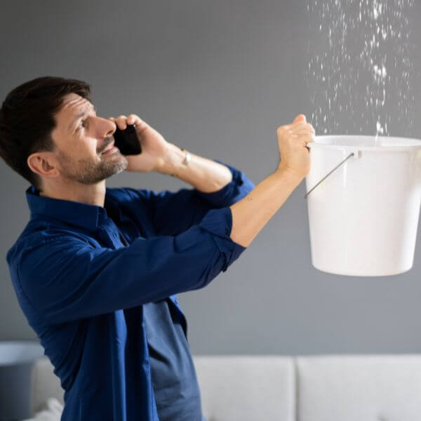 Business owner holding a bucket under a ceiling leak while calling Roofing Guys Melbourne for urgent commercial roof repairs and leak detection in Melbourne. Business owner holding a bucket under a ceiling leak while calling Roofing Guys Melbourne for urgent commercial roof repairs and leak detection in Melbourne.